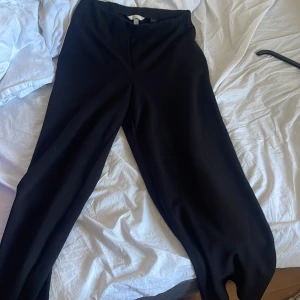 Svarta wide kostymbyxor  - Snygga svarta kostymbyxor från H&M i storlek M. Byxorna har hög midja och ett wide ben som ger en chill och modern siluett. Materialet är mjukt och består av polyester och elastan, vilket gör dem bekväma och följsamma. Perfekta för en clean och stilren look.
