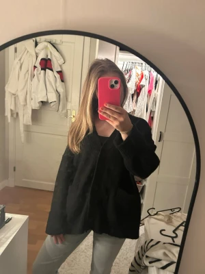 Svart kofta från Monki - Klassisk svart kofta från Monki med v-ringad hals, tre knappar framtill och två fickor. Koftan är ribbad vid ärmslut och nederkant och har en loose passform. Perfekt att slänga över en t-shirt eller topp för en chill look. Använd 2ggr