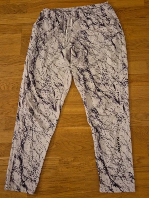 Vita mjukisbyxor med marmormönster - Säljer ett par vita mjukisbyxor med svart marmormönster och dragsko i midjan. Byxorna har avslappnad passform och resår i midjan för extra komfort. Perfekta för chill dagar eller när du vill ha en unik stil.