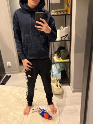 Mörkblå hoodie med huva - Säljer en mörkblå hoodie med huva och dragsnören. Hoodien har en stor magficka framtill och ribbade muddar vid ärmslut och nederkant. Perfekt för en avslappnad och stilren look. Materialet känns mjukt och bekvämt.