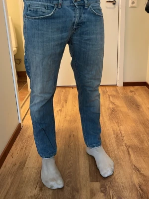 Dondup jeans - Säljer ett par blå jeans med rak passform och klassisk femficksdesign. Jeansen har dragkedjedetaljer på bakfickorna och en snygg tvättad look. Perfekta för dig som gillar en avslappnad stil och vill ha något som funkar till det mesta.