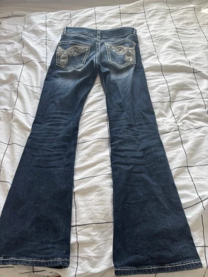 Blå bootcut jeans från Gina Tricot - Säljer ett par mörkblå bootcut jeans från Gina Tricot med snygga detaljerade bakfickor och kontrastsömmar. Jeansen har låg midja och klassisk femficksdesign. Perfekta för dig som gillar en retro och avslappnad stil.