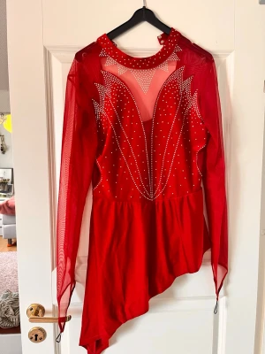 Röd meshklänning med stenar - Röd konståkningsklänning med asymmetrisk kjol och meshtyg. Storlek M 