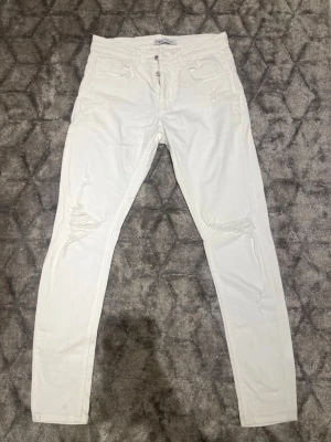 Vita ripped skinny jeans från Zara - Säljer ett par vita skinny jeans från Zara med slitningar på båda knäna och klassisk femficksdesign. Jeansen har hög midja, knappgylf och är tillverkade i stretchigt material för en bekväm passform. Perfekta för en trendig och avslappnad look.👀 Skickas inom 24h! 💬 Priset kan diskuteras vid snabb köp.