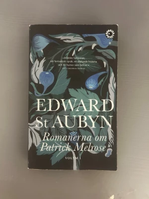 Romanerna om Patrick Melrose Volym I - En tjock pocketbok med svart omslag och stiliserade blå och gröna blommor. Titeln och författarnamnet är tryckta i stora vita bokstäver. Perfekt för dig som gillar modern skönlitteratur med djup och humor.