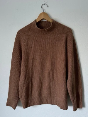 Brun stickad tröja med hög hals - Mysig brun stickad tröja med rak passform och hög hals. Tröjan har långa ärmar och är ribbstickad i ett mjukt material, perfekt för kyliga dagar. Enkel och stilren design utan synliga loggor eller detaljer. 8A8