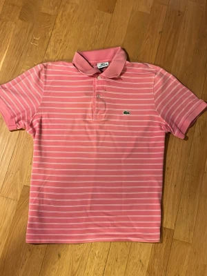 Rosa Lacoste piké - Säljer en Lacoste piké med fint mönster, den är i storlek S och har 60 cm emellan början av kragen och botten av tröjan, skriv till mig vid minsta fundering eller fråga!