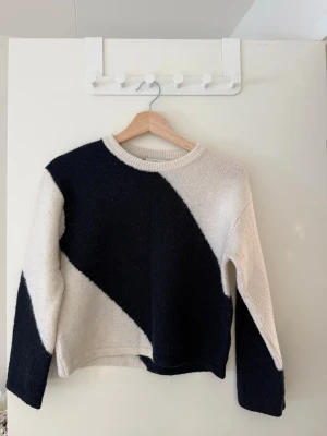 Marinblå och vit stickad tröja med diagonal design - stickad tröja i marinblått och vitt med breda diagonala block över hela plagget. Tröjan har rund halsringning med långa ärmar.