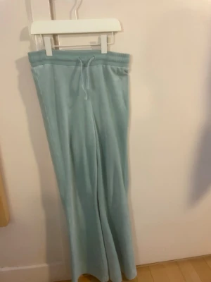 Mintgröna mjukisbyxor med utsvängda ben - Snygga mintgröna mjukisbyxor med utsvängda ben och dragsko i midjan. Byxorna är gjorda i ett mjukt och skönt velourmaterial som känns riktigt bekvämt. Perfekta för en chill och avslappnad stil.