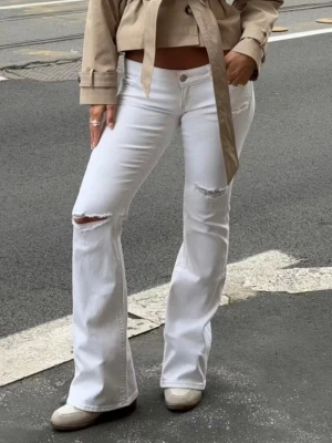 Vita bootcut jeans med slitningar 14+ petite - Säljer ett par vita bootcut jeans med slitningar över knäna och lätt utsvängda ben. Jeansen har klassisk femficksdesign och normal midja. Perfekta för dig som vill ha en trendig och avslappnad look.