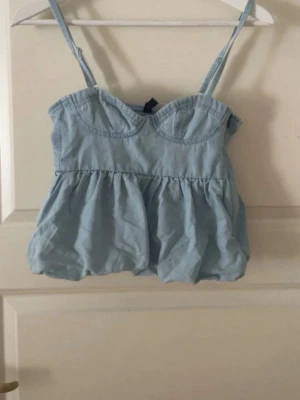 Ljusblå jeanstopp med volang - Supersöt ljusblå topp med volang och smala axelband. Toppen har en markerad byst och en luftig, flowy passform som ger en romantisk vibe. Säljer då den var för liten i storlek. Köpt här på plick men har inte använt den 💕