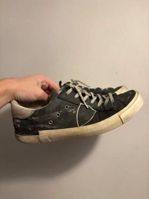 Svarta låga sneakers med vita detaljer - Svarta sneakers med vita sulor och detaljer. Skorna har vita snören och metallhål för snörningen. Yttermaterialet ser ut att vara läder eller konstläder. Klassisk låg modell som passar till jeans eller streetwear.