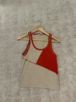 Ribbad linnetopp från Zara - Säljer en ribbad linnetopp från Zara i beige och rött. Toppen har ett coolt geometriskt mönster med breda axelband och rund halsringning. Perfekt för varma dagar och enkel att styla med jeans eller kjol.