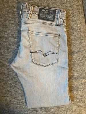 Replay Anbass Slim Fit ljusblå jeans - Snygga ljus grå jeans från Replay, modell Anbass Slim Fit. Jeansen har klassisk femficksdesign, coola kontrastsömmar på bakfickan och en bekväm passform. Perfekta för dig som gillar en modern och stilren look.
