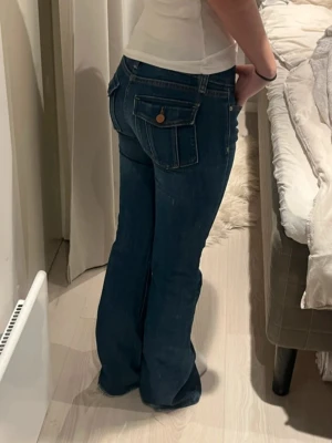 Lågmidjade vintage bootcut jeans med coola fickor  - Snygga mörkblå jeans med bootcut-modell och stora fickor bak med knappdetalj. Jeansen har klassisk femficksdesign och är tillverkade i ett stretchigt denimtyg som sitter skönt på kroppen. Perfekta för dig som gillar en retroinspirerad look. Jag är 160 som referens!