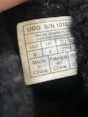 Svarta UGG tofflor i fårskinn - Mysiga svarta UGG tofflor i äkta fårskinn med mjuk insida och klassisk kort modell. Perfekta för att hålla fötterna varma hemma eller ute. Tidlös design med grov sula och synliga sömmar. Storlek 37 EU.