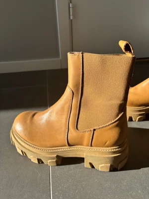 Chunky bruna Chelsea boots i skinn - Säljer ett par snygga Chelsea boots i brunt skinn med chunky sula och elastiska paneler på sidorna. Bootsens robusta design och dragflik bak gör dem både stilrena och praktiska. Perfekta för dig som gillar en trendig och avslappnad look. Nypris 1300