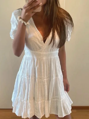 Vit omlottklänning från Zara - Söt vit kortklänning från Zara med omlottdesign och puffärmar. Klänningen har v-ringning, volangdetaljer och är tillverkad i ett lätt bomullstyg. Perfekt för studenten men också bara en vanlig sommardag 