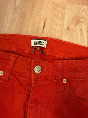 Röda skinny jeans från Tommy Jeans - Snygga röda skinny jeans från Tommy Jeans med låg midja. Klassisk femficksmodell med detaljer i silver och en liten ficka med Tommy Hilfiger-flagga. Perfekta för dig som vill sticka ut med färg.