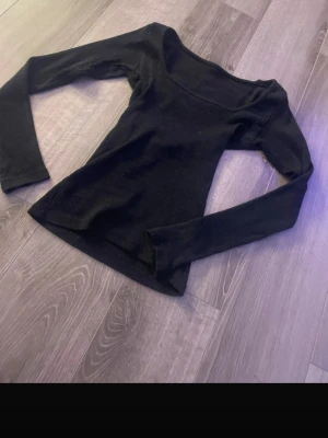 Svart ribbad långärmad topp - En svart, ribbad långärmad topp med fyrkantig ringning. Sitter tight och är perfekt att styla med jeans eller kjol. Mjuk och stretchig, passar dig som gillar en enkel men snygg look.