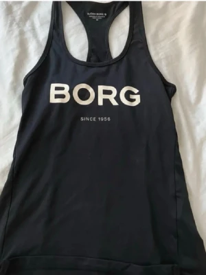 Svart träningstopp från Björn Borg - Snygg svart träningstopp från Björn borg. Modellen har brottarrygg och är tillverkad i ett stretchigt funktionsmaterial som passar för gym eller löpning.