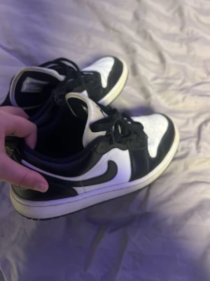 Svarta och vita Air Jordan 1 Low - Säljer ett par Air Jordan 1 Low i svart och vitt läder. Klassisk siluett med broderad Air Jordan-logga på hälen och vit sula. Perfekta för dig som gillar streetwear och sneakers med ikonisk design.