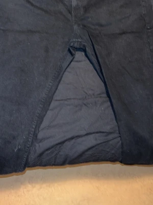 Svarta raka jeans med bakfickor - Säljer ett par svarta jeans med raka ben och klassiska bakfickor. Jeansen har en enkel design utan synliga loggor och är tillverkade i ett kraftigt denimtyg. Perfekta för dig som gillar en clean och stilren look.