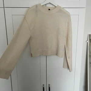 Beige stickad tröja med rund hals - En enkel och stilren beige stickad tröja med rund hals och långa ärmar. Tröjan har ribbade muddar vid ärmslut och nederkant samt en något boxig passform. Perfekt att matcha med jeans eller kjol för en avslappnad look.