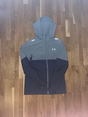 Under armour windbreaker - Säljer en snygg och funktionell löparjacka från Under Armour. Jackan är i utmärkt skick, ser ut som ny och knappt använd! Perfekt för löpning och andra utomhusaktiviteter. Den är lätt, andas bra och skyddar mot vind och lätt regn.  *   Märke: Under Armour *   Skick: Som Ny *   Egenskaper: Lätt, andas, vind- och vattenavvisande *   Passar perfekt: Löpning, träning, vardagsbruk  Om du är intresserad, tveka inte att höra av dig! 