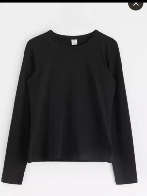 Svart långärmad topp i bomull - En basic svart långärmad topp med rund halsringning. Tillverkad i mjuk bomull som känns skön mot huden. Perfekt att styla lager på lager eller bära som den är. Enkel och stilren design utan detaljer.