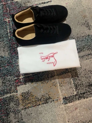 Svarta sneakers från Christian Louboutin - Stilrena svarta sneakers från Christian Louboutin med lågt skaft och klassisk design. Skorna har svarta snören, diskret logga på insidan och beige innersula. Perfekta för dig som gillar exklusiva och tidlösa sneakers.