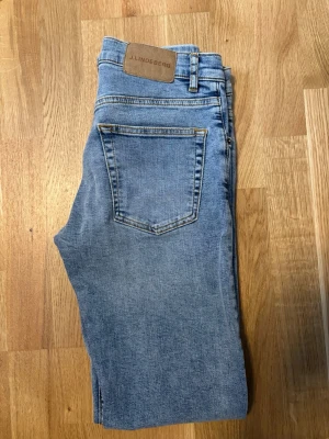 Ljusblå slim jeans från J.Lindeberg - Snygga ljusblå jeans från J.Lindeberg med klassisk femficksdesign och slim passform. Jeansen har en patch med logga bak i midjan och är tillverkade i mjukt denimtyg. Perfekta för en avslappnad och trendig look.