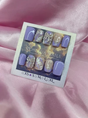 Lilac (S);Short Ballerina - Säljer handgjorda press-on naglar i lila och nude toner. Naglarna har coola vita och silverfärgade dekorationer som rosetter, stjärnor och swirl-mönster. Formen är ballerina och korta. Perfekt för dig som vill ha unika och snygga naglar!S: 15 mm, 11,5 mm, 12 mm, 11 mm, 9 mm 
