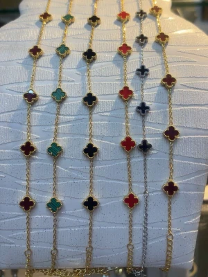 Färgglada klöverarmband i guldton - Säljer flera armband med fyrklöverformade hängen i olika färger som rött, grönt, svart och mörkblått. Armbanden har tunna kedjor i guldfärgad metall och varje hänge är inramat med små guldfärgade detaljer. Perfekt för dig som gillar färg och unika accessoarer.