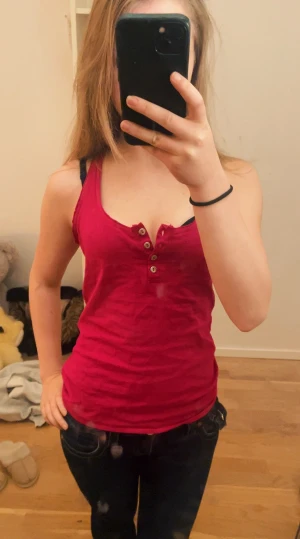 Röd ärmlös linnetopp med knappar - Snygg röd linnetopp med knappar där framme, toppen är ärmlös och har en tight passform som framhäver figuren. Perfekt att matcha med jeans eller kjol. Det finns ingen storlek på tröjan och den är köpt second hand men jag brukar ha xxs-s i tröjor, knapparna går att knäppa, skriv för frågor eller bilder! 🩷 pris är diskuterbart! ⭐️💝