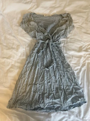 Blå blommig omlott klänning  - Supersöt blå klänning med små vita blommor och volangdetaljer vid halsen. Perfekt för sommaren. Från marknad i Spanien därav ingen lapp med storlek , men skulle säga att de är S. Knappt använd, skrynklig pga den varit vikt så länge 