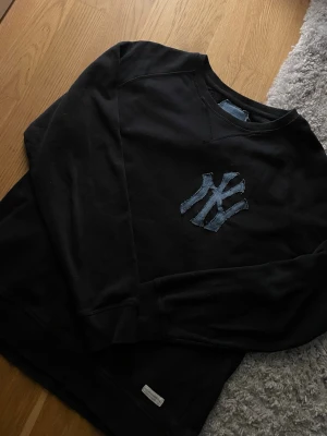 Svart sweatshirt med NY-logga (gjord själv) - Gjord själ! Cool svart sweatshirt med stor NY-logga i denim på bröstet. Tröjan har rund halsringning och långa ärmar. Perfekt för dig som gillar streetwear och vill ha en avslappnad stil. Sitter som S