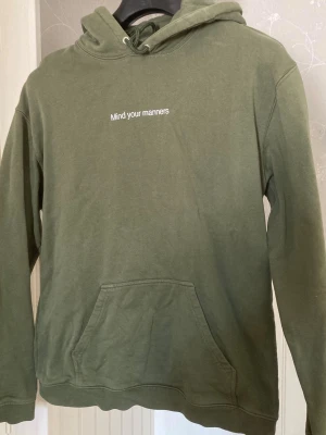 Olivgrön hoodie med text - Snygg olivgrön hoodie med vit text 'Mind your manners' på bröstet. 