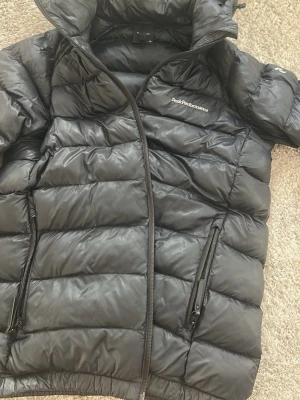 Svart dunjacka Peak Performance - Säljer en svart dunjacka från Peak Performance med hög krage och två dragkedjeförsedda fickor. Jackan har quiltad design och är fylld med dun för extra värme. Perfekt för kalla vinterdagar och är i storleken 170 men passar som xs.