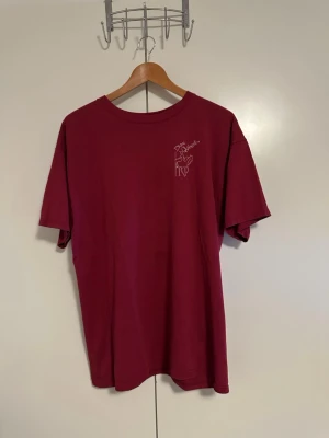 Vinröd Don Quixote t-shirt - Säljer en vinröd t-shirt med tryck från Don Quixote-föreställningen av Joan Harris Dancers. T-shirten har rund hals, korta ärmar och ett vitt motiv både fram och bak. Perfekt för dig som vill ha en unik t-shirt med coolt tryck.