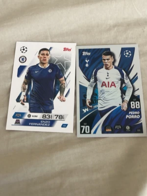 Match Attax fotbollskort Chelsea & Spurs - Två Match Attax samlarkort från Topps med fotbollsspelare från Chelsea FC och Tottenham Hotspur. Ena kortet visar Enzo Fernandez i blå Chelsea-tröja och det andra Pedro Porro i vit Tottenham-tröja. Perfekt för dig som samlar på fotbollskort!