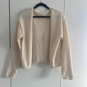 Beige stickad kofta - Mysig beige stickad kofta med små knappar och långa ärmar. Koftan har en enkel, rak passform och ribbade muddar vid ärmslut och nederkant. Perfekt att slänga över en t-shirt för en avslappnad look. Finns inga lappar i den men den är i S. 