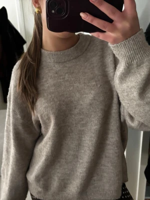 Beige stickad tröja med rund hals - Mysig beige stickad tröja med rund halsringning och ribbade muddar vid ärmslut och nederkant. Tröjan har en avslappnad passform och är perfekt för lager på lager. Passar till allt och är superenkel att styla.