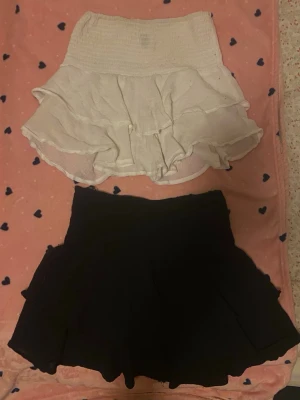 Volangkjol - Säljer två söta korta kjolar från SHEIN, en i vit och en i svart. Båda har volangdetaljer och elastisk midja som ger en skön passform. Perfekt för dig som gillar en feminin och trendig look. Materialet känns lätt och luftigt. Den vita är i storlek XS och den svarta är i M. En för 70 2 för 100🤍