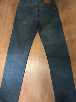 Levi's raka blå jeans - Klassiska blå jeans från Levi's med rak passform och fem fickor. Jeansen har en vintage look med lätt slitning och är tillverkade i denim av bomull. Perfekta för en avslappnad och tidlös stil.