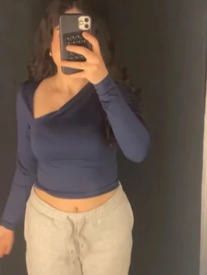 Marinblå oneshoulder topp - Trendig marinblå oneshoulder topp med lång ärm och croppad passform. Snygg asymmetrisk skärning. Perfekt att styla med både jeans och kjol för en modern look.