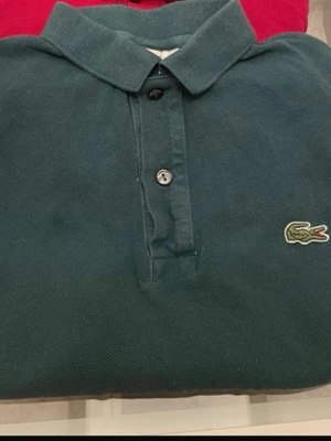 Mörkgrön pikétröja från Lacoste - Klassisk mörkgrön pikétröja från Lacoste med slim fit-passform. Tröjan har krage, knappar framtill och den ikoniska krokodilloggan broderad på bröstet. Perfekt för en clean och stilren look.