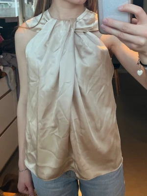 Elegant satinblus  - Jättefin elegant ärmlös blus i champagnefärgad satin. Otroligt fin topp i jättefint skick utöver att den är aningen skrynklig på bilderna. Storlek S!! Skriv för frågor och kolla in min profil!!