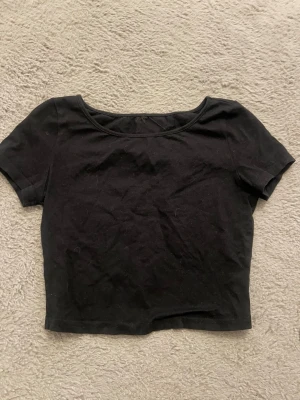 Svart croppad topp med kort ärm - En enkel svart croppad topp med rund halsringning och korta ärmar. Perfekt att matcha med höga jeans eller kjol för en clean och stilren look. Tillverkad i mjuk bomull som känns skön mot huden. Aningen tajt på mig som brukar ha S
