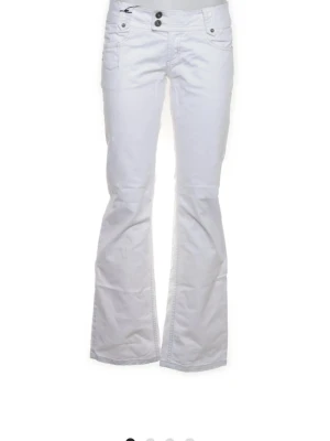 Vita bootcut jeans med låg midja - Skit Snygga vita bootcut jeans med låg midja och dubbla knappar fram. Klassiska femficksmodellen och utsvängda ben ger en retrovibe. Perfekta för dig som vill sticka ut med en fräsch och clean look. Materialet känns mjukt och följsamt.